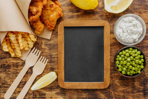 Top view of fish and chips in paper wrap with peas and chalkboard