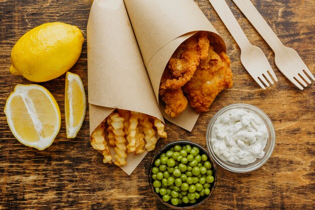 Top view of fish and chips in paper wrap with peas and cutlery