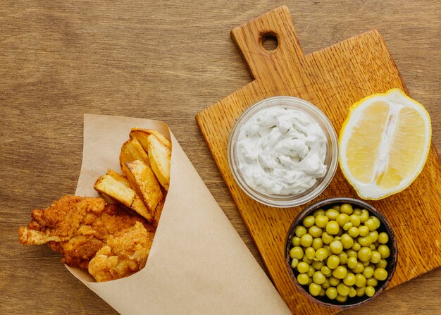 Vista dall'alto di fish and chips in involucro di carta con piselli e fetta di limone