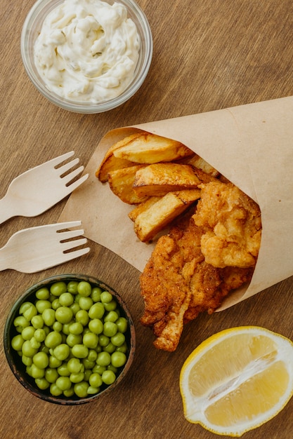 Top view of fish and chips in paper wrap with peas and sauce