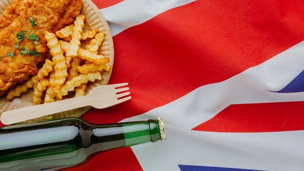 Вид сверху рыбы с жареным картофелем на тарелке с пивной бутылкой и флагом великобритании