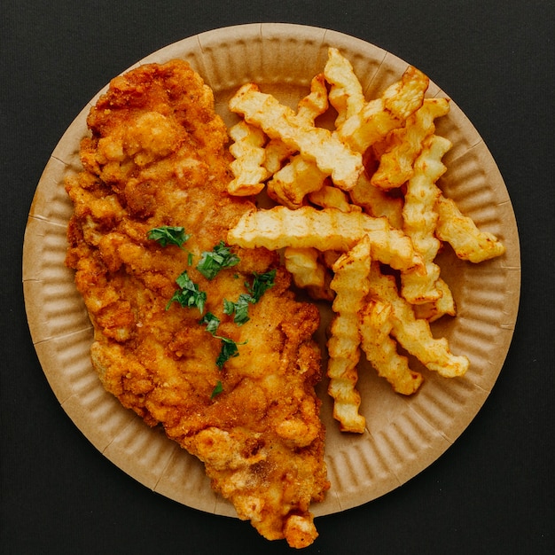 Вид сверху рыбы с жареным картофелем на тарелке с зеленью