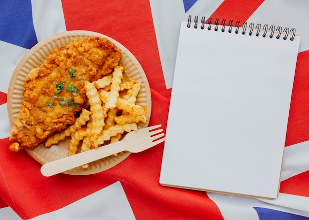 Free photo top view of fish and chips on plate with notebook and great britain flag