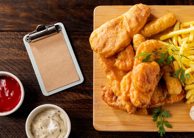 Top view of fish and chips with clipboard and sauces