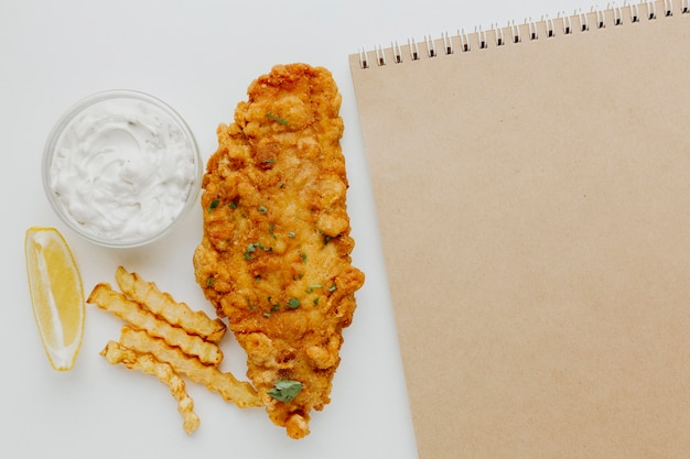 Top view of fish and chips with sauce and notebook