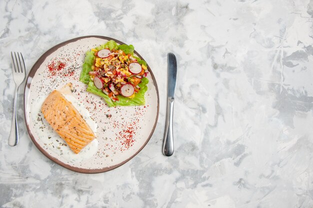 스테인드 흰색 표면의 왼쪽에 설정된 접시와 칼에 생선 식사와 맛있는 샐러드의 상위 뷰