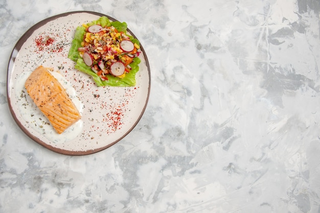 Top view of fish meal and delicious salad on a plate on stained white surface