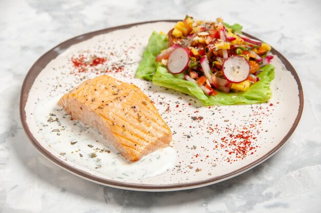 Top view of fish meal and salad on a plate on stained white surface