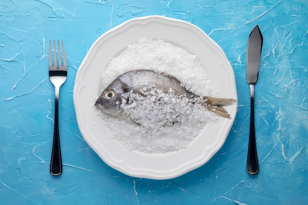 Top view of fish on plate with salt and cutlery