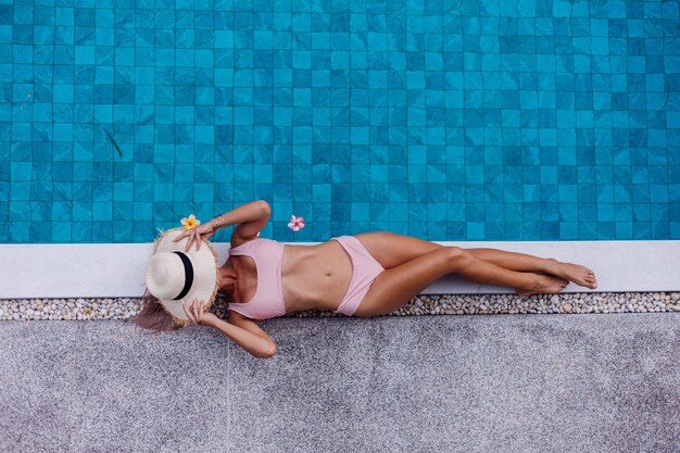 Top view of fit slim woman in bikini on edge of swimming pool enjoying vacation