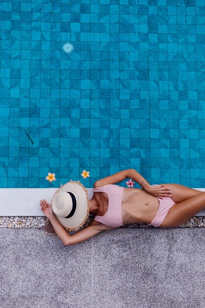 Top view of fit slim woman in bikini on edge of swimming pool enjoying vacation