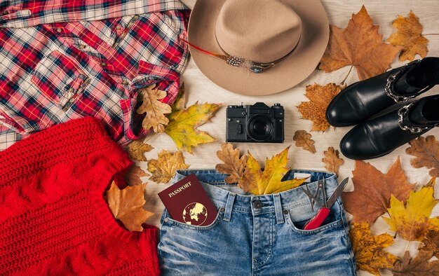 Top view on flat lay of woman style accessories, red sweater, checkered flannel shirt, jeans, black leather boots, autumn fashion trend, vintage photo camera, swiss knife, passport, traveler outfit