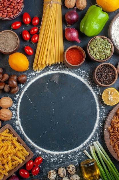 Top view flour circle around eggs vegetables pasta nuts and seasonings on dark background photo color raw meal health food
