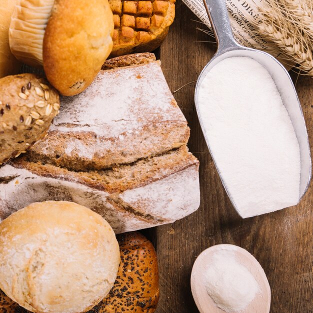 Top view of flour in shovel with baked whole breads and cake on wooden table