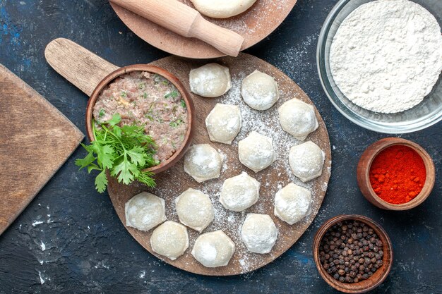 Top view of floured dough pieces with minced meat greens along with pepper on dark desk, dough food raw meat dinner pastry