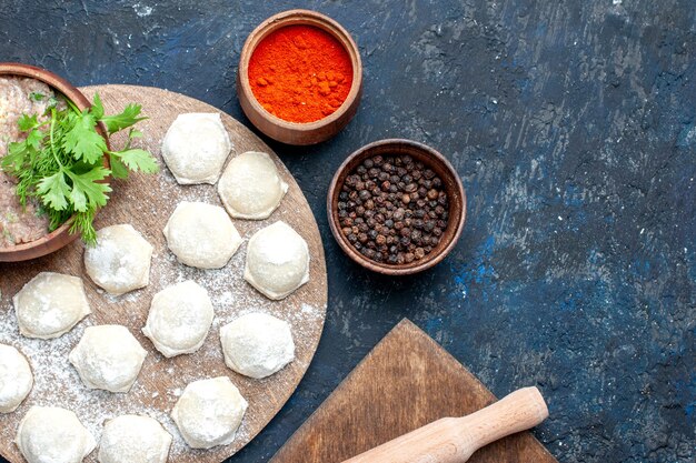 Top view of floured dough slices with minced meat greens and peppers on dark desk, food raw meat dinner pastry