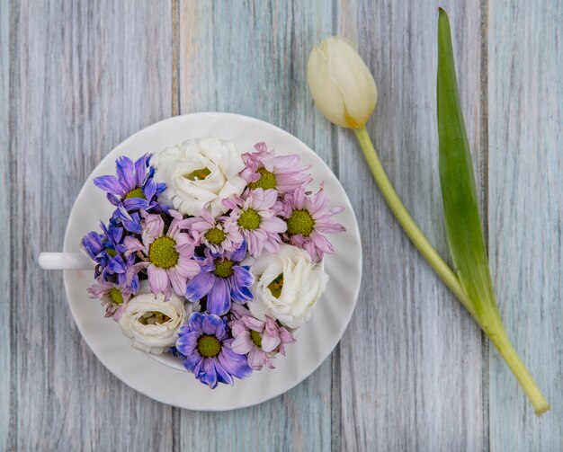 Top view of flowers in cup on saucer and on wooden background