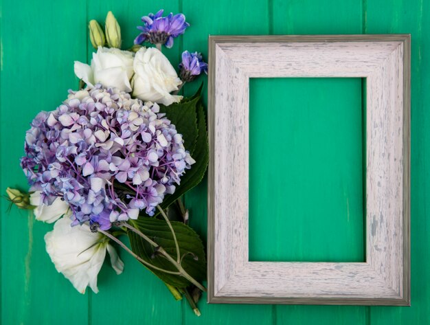 Top view of flowers and frame on green background with copy space