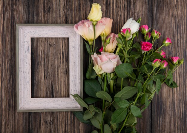 Top view of flowers and frame on wooden background with copy space