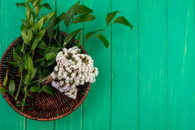 Top view of flowers with leaf branches in a basket on a green surface