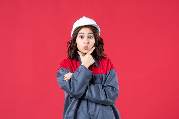 Top view of focused female builder in uniform with hard hat and concentrated on something on isolated red background