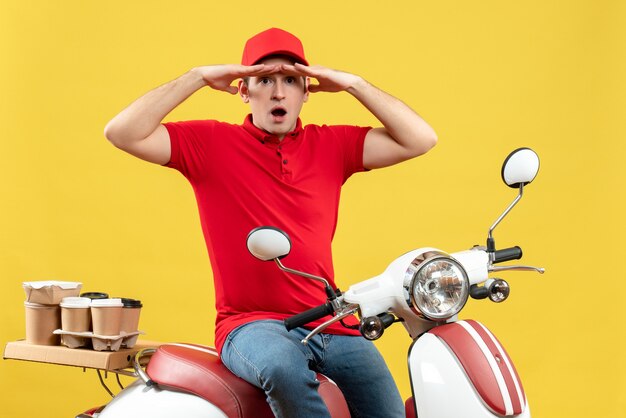 Top view of focused young guy wearing red blouse and hat delivering orders on yellow background