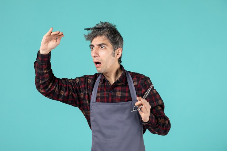 मुफ़्त फोटो top view of focused young hairdesser wearing gray apron and holding comb and scissor on pastel blue color background