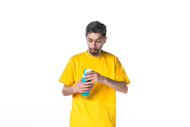 白い表面に魔法瓶を保持している黄色のシャツに焦点を当てた若い男性の上面図