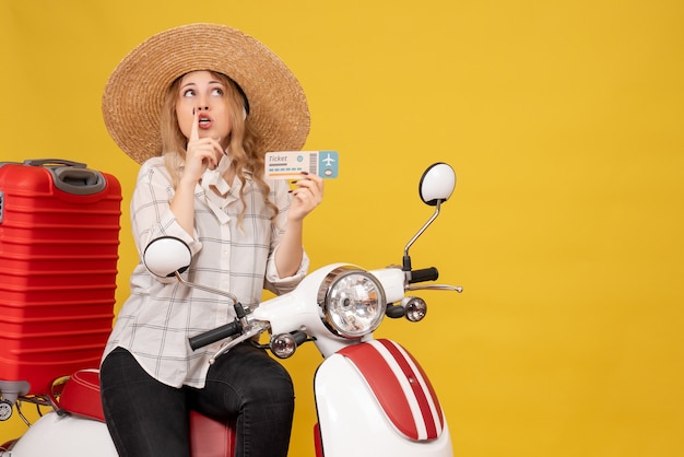 Top view of focused young woman wearing hat and sitting on motorcycle and holding ticket looking up on yellow 