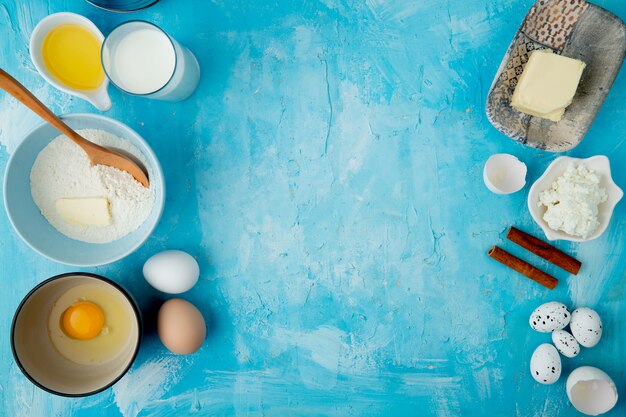 Вид сверху продуктов, как мука, масло, молоко, творог, корица и яйцо на синем фоне с копией пространства