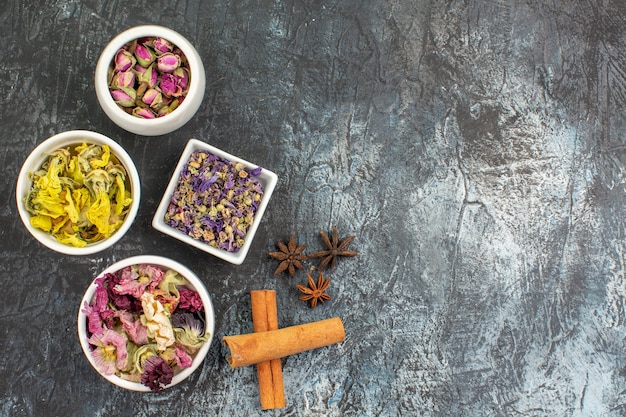 Free photo top view of four bowls of dry flower and cinnamon sticks and anise on grey background