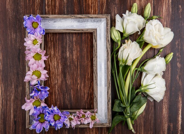 Top view of frame and flowers on it and on wooden background with copy space