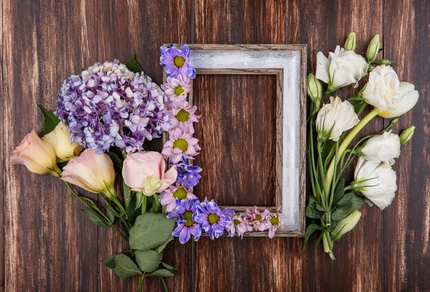 Top view of frame and flowers on it and on wooden background with copy space