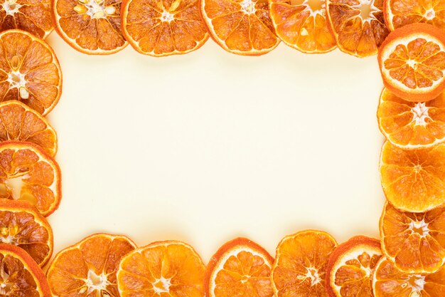 コピースペースと白い背景の上に配置された乾燥したオレンジスライスで作られたフレームのトップビュー