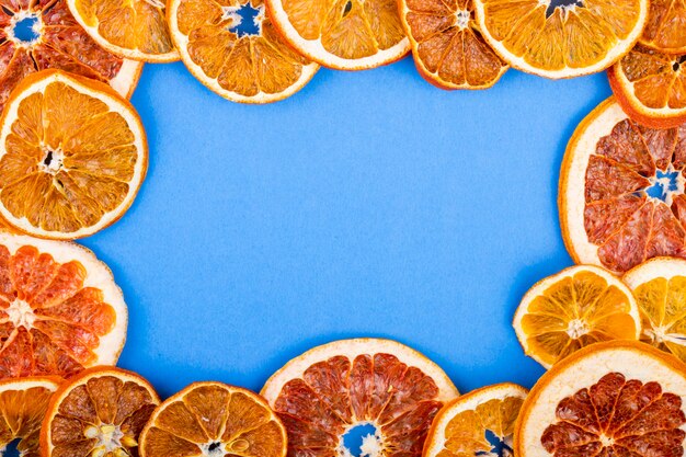 Top view of a frame made of dried slices of orange and grapefruit arranged on blue background with copy space