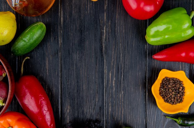 Top view of a frame made of fresh vegetables colorful bell peppers green chili peppers cucumber tomato and black peppercorns on dark wood with copy space