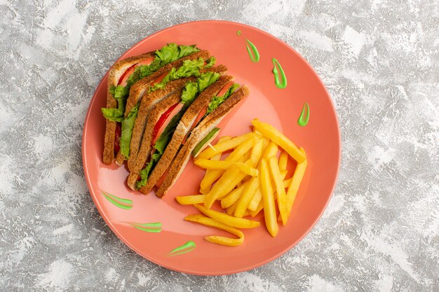 Top view of french fries along with sandwiches inside peach plate