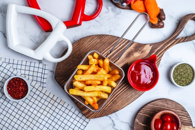 Top view french fries in a basket with ketchup on the board