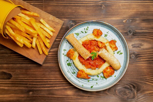 Top view of french fries with chicken slices on brown table