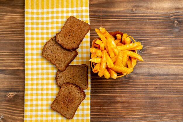 Top view of french fries with dark bread loafs on brown table potato bread meal burger food
