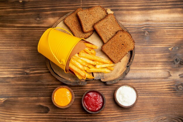 Top view of french fries with dark bread and seasonings on brown table