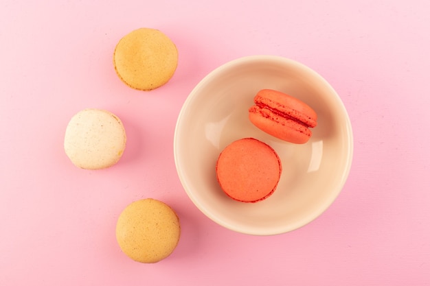 A top view french macarons colored inside and outside plate on the pink table cake biscuit sugar sweet