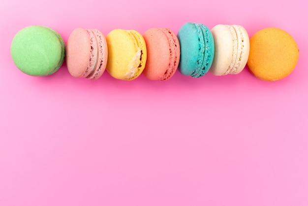 A top view french macarons colorful round delicious lined on pink, cake biscuit confectionery
