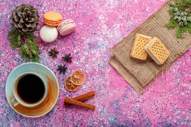 Top view french macarons delicious little cakes with tea and waffles on the pink surface