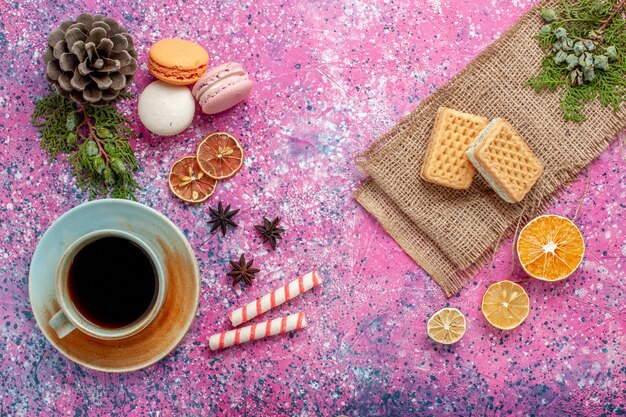 Top view french macarons delicious little cakes with waffles and tea on the pink surface