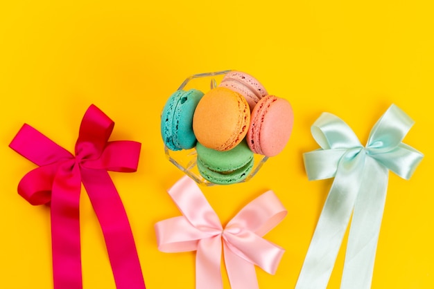 A top view french macarons round sweet with colorful bows on yellow, cake confectionery sweet sugar