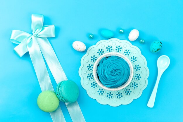 A top view french macarons with colorful eggs white, plastic spoon on blue, cake biscuit color