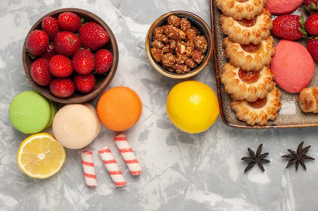 Top view french macarons with fresh red strawberries and cookies on white surface