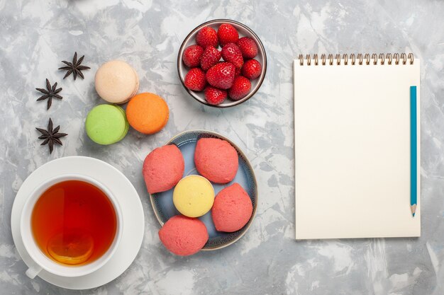 Top view french macarons with little cakes and cup of tea on the white surface cake biscuit sugar sweet pie tea