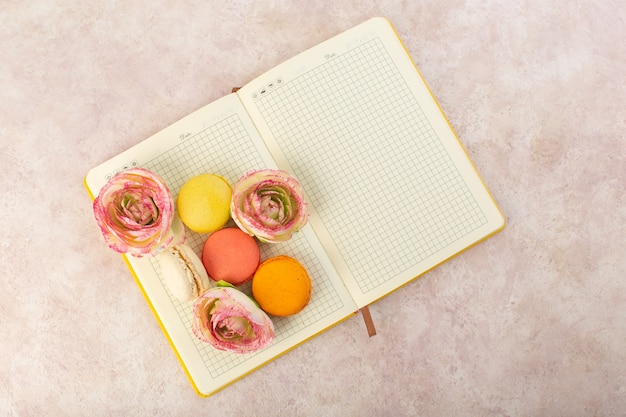 A top view french macarons with roses on the copybook and pink table cake biscuit sugar sweet